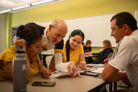 Students and teacher conversing over paperwork in adult basic skills class