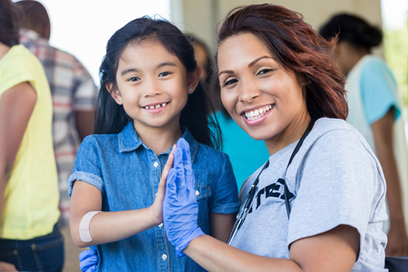 Public health employee high fiving a young girl with a bandaid on her armerials at a table