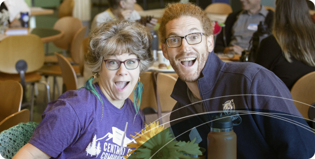 Two happy smiling COCC employees seated at a lunch table