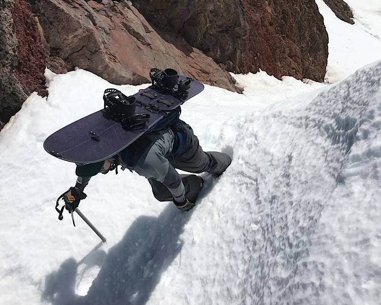 Snowboarder ckimbing a tight chute with ice axe