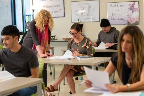 Faculty member works with a student at a desk in the classroom