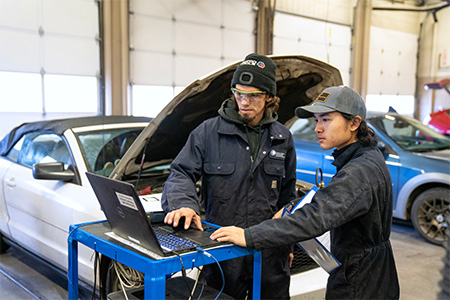 Two COCC Automotive Technology students working on a car with the hood open.