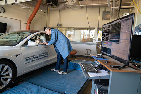 A COCC Automotive student in a test car while a teacher stands outside it.