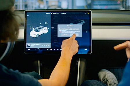 Two students in a car pointing at a screen.