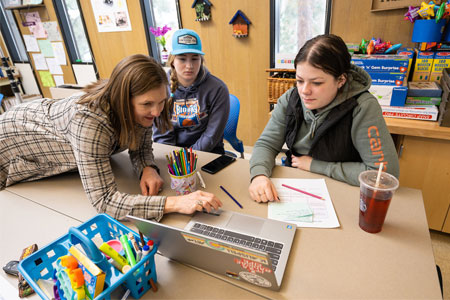 Education faculty member teaching two femaile students huddled around a laptop computer