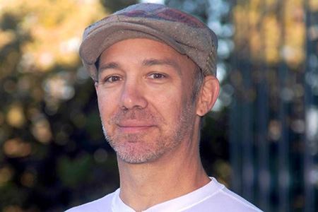 Headshot of faculty member Alan Nunes. Male wearing a newsboy style hat.