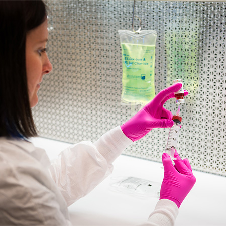 A woman in a lab coat using a syringe to extract liquid from a glass bottle.