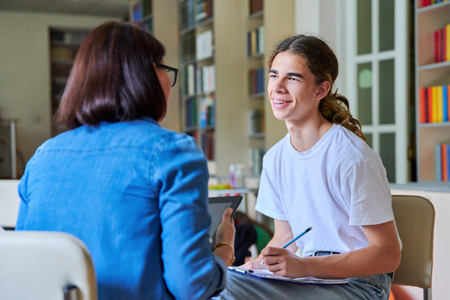 Woman and male student talking in a psychological setting while student takes notes.