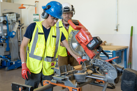 Teacher showing students how to operate machinery in apprenticeship facility